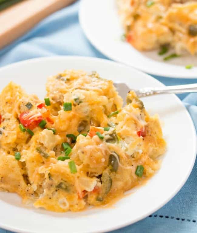 A white bowl filled with soft scrambled eggs topped with diced chives.