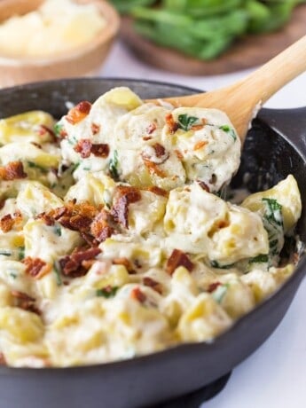 A spoon scooping out tortellini al forno from a black cast iron skillet.
