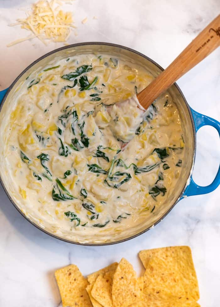 Spinach and Artichoke Dip in a Dutch oven on white granite with chips and cheese