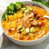 A bowl of Creamy Chicken Tortilla Soup topped with crispy tortillas and garnished with avocados, cheese, jalapenos, and cilantro.