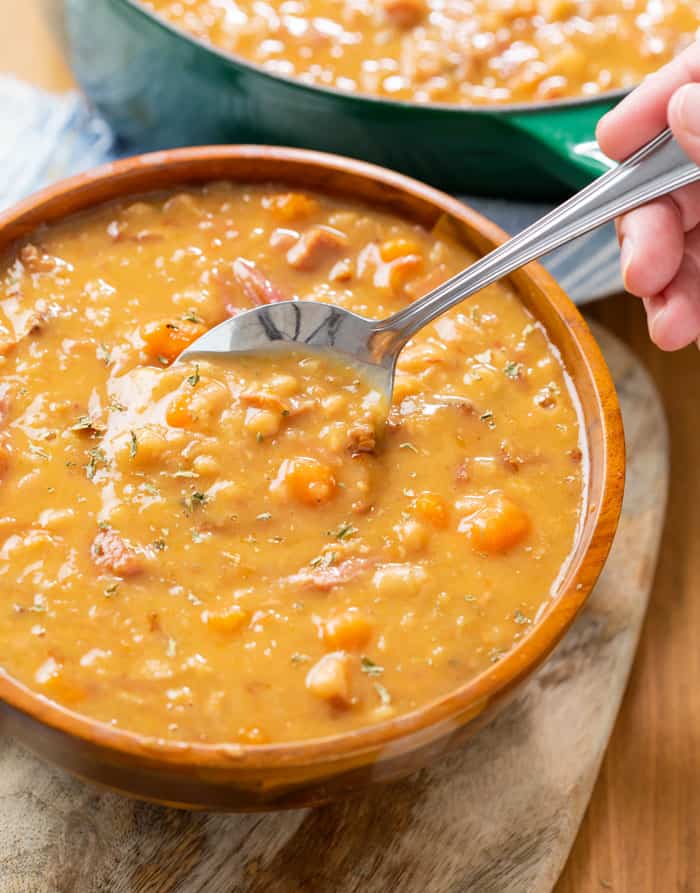 A wooden bowl full of ham and bean soup with a spoon.