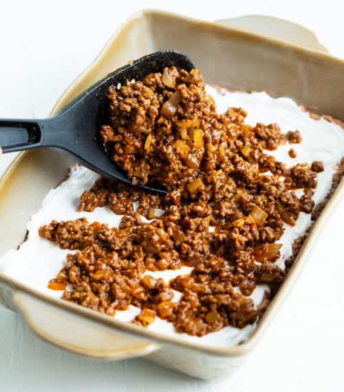 A big spatula spooning seasoned ground beef into a casserole dish for taco casserole.