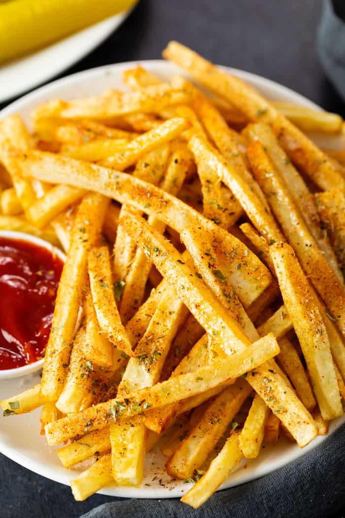 A plate of seasoned french fries on a white plate next to a bowl of ketchup.