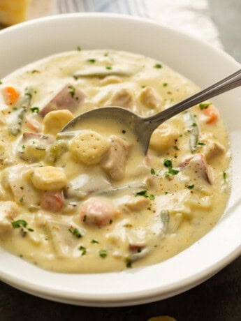 A spoon scooping up creamy chicken stew topped with oyster crackers.
