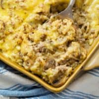 A spoon holding a scoop of cheesy ground beef and rice casserole in a casserole dish.