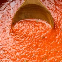 A wooden spoon scooping up homemade marinara sauce from a pot.
