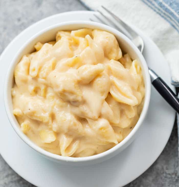 A white bowl of Panera mac and cheese on a white plate with a fork .