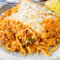 A plate with a slice of baked spaghetti topped with mozzarella cheese and a fork in the background.