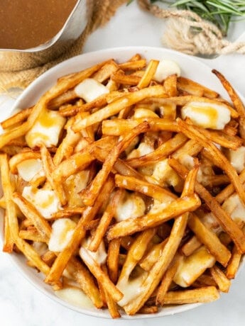 A white plate full of homemade poutine with french fries, gravy, and melted cheese curds.