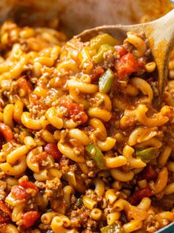 A wooden spoon stirring a pot of hot American Chop Suey.