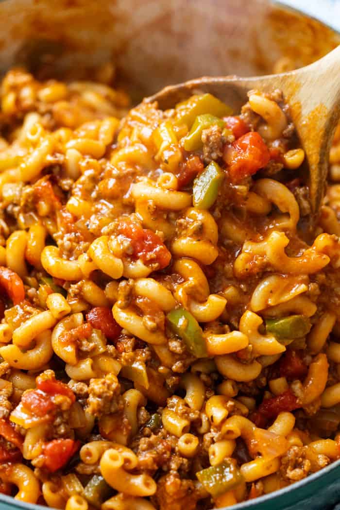 A wooden spoon stirring a pot of hot American Chop Suey.