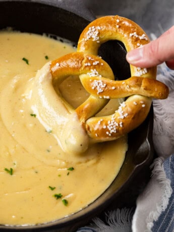 A cast iron skillet with beer cheese dip with a soft pretzel being dipped in it.