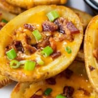 A pile of potato skins topped with cheese, bacon, and green onions.