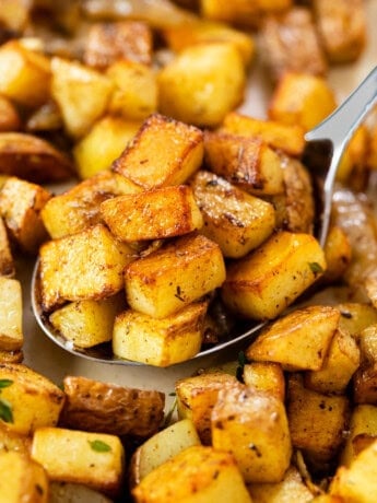A large metal spoon full of crispy skillet potatoes.