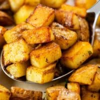 A metal spoon holding crispy skillet potatoes in a pan.
