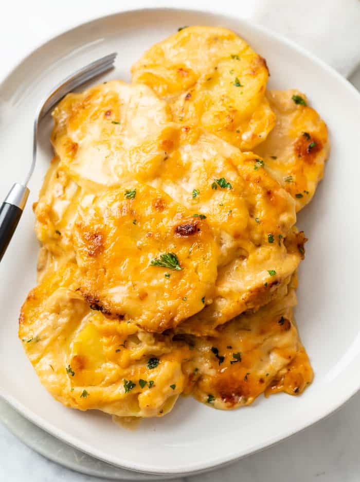 A white plate with Cheesy Scalloped potatoes on top and a fork on the side.