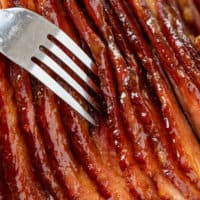 A fork in between slices of Glazed Ham cut into thin slices.