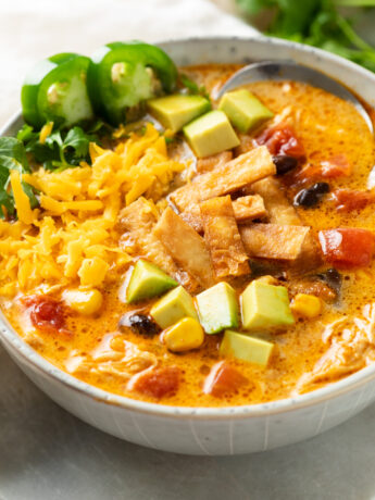 Chicken Tortilla Soup in a soup bowl with colorful toppings and a spoon in the back.