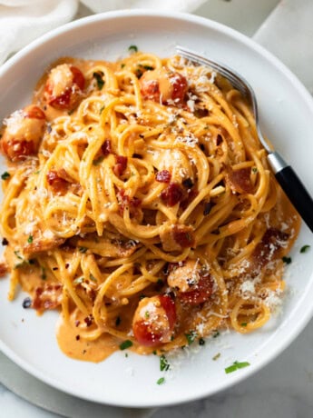 A white plate with creamy bacon pasta on it with spaghetti and crispy bacon.
