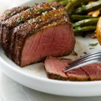 Filet Mignon on a plate with a slice taken from it and a fork in front.