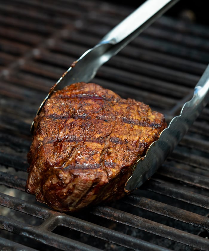 Filet Mignon on the grill with grill tongs around it.