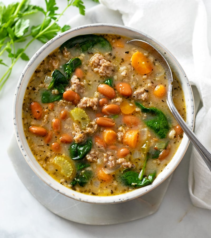 A soup bowl filled with Pinto Bean Soup with a spoon on the side.