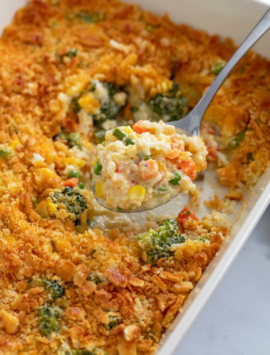 A spoon scooping up Vegetable Casserole from a baking dish.