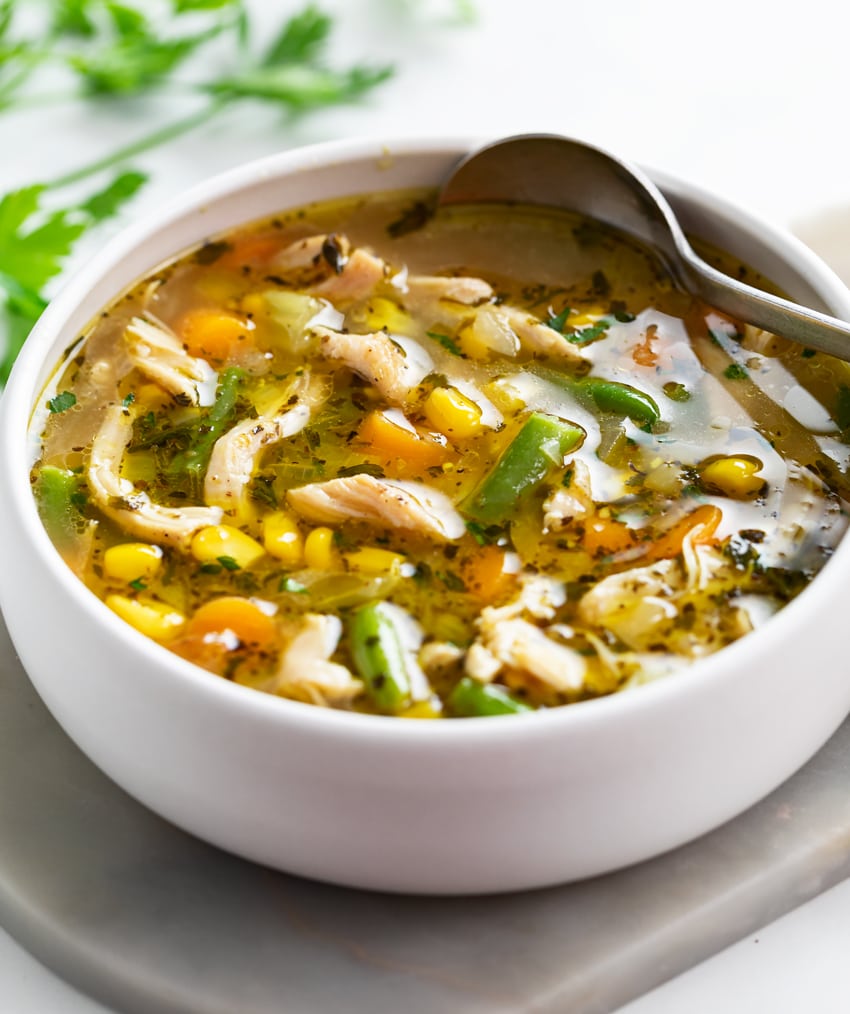 A white bowl filled with Chicken Vegetable Soup with a spoon.