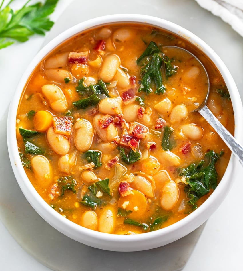 A white soup bowl filled with White Bean Soup with a spoon in it.
