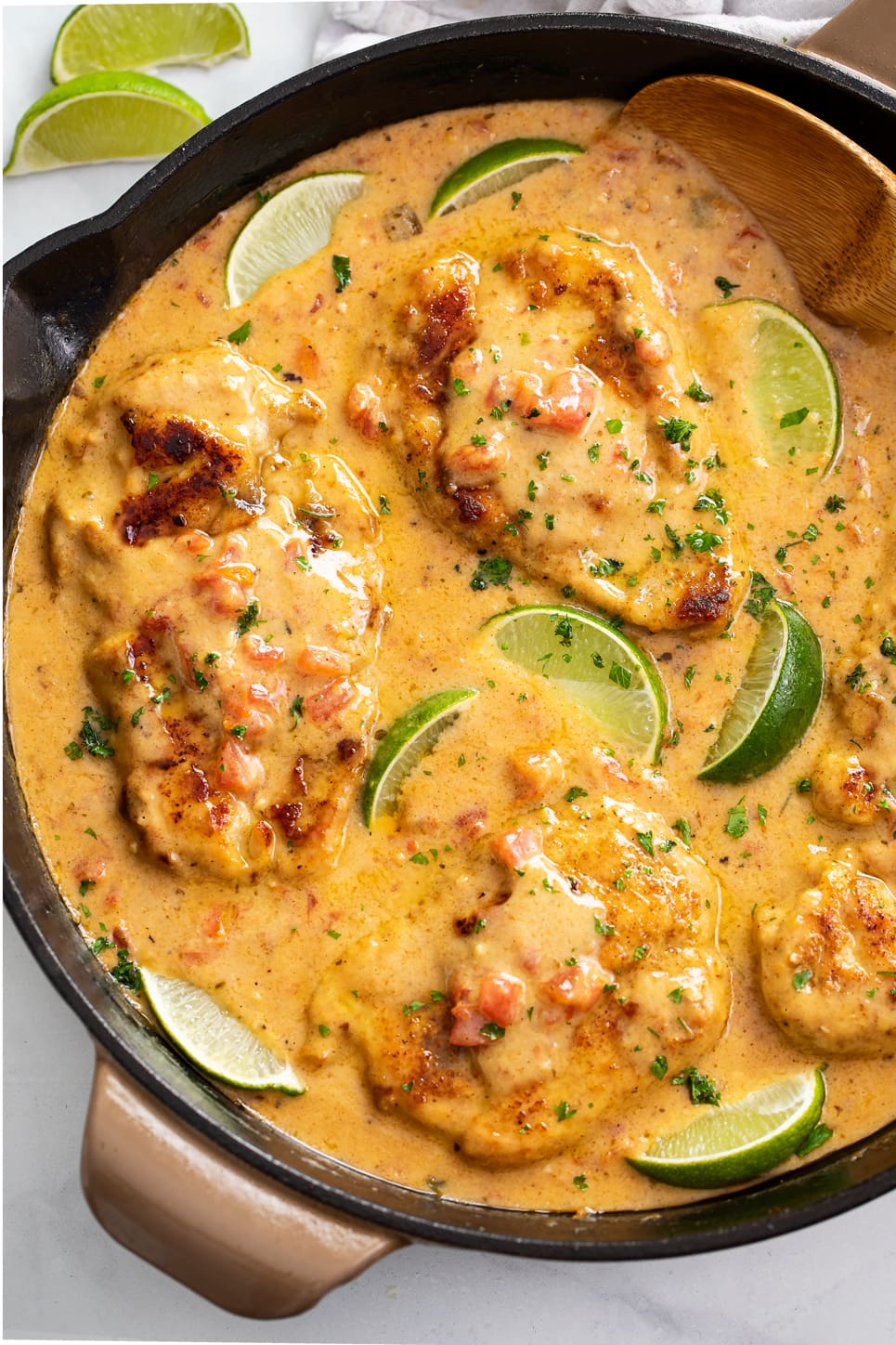 A skillet of Cajun Chicken in a sauce with cilantro and lime wedges.