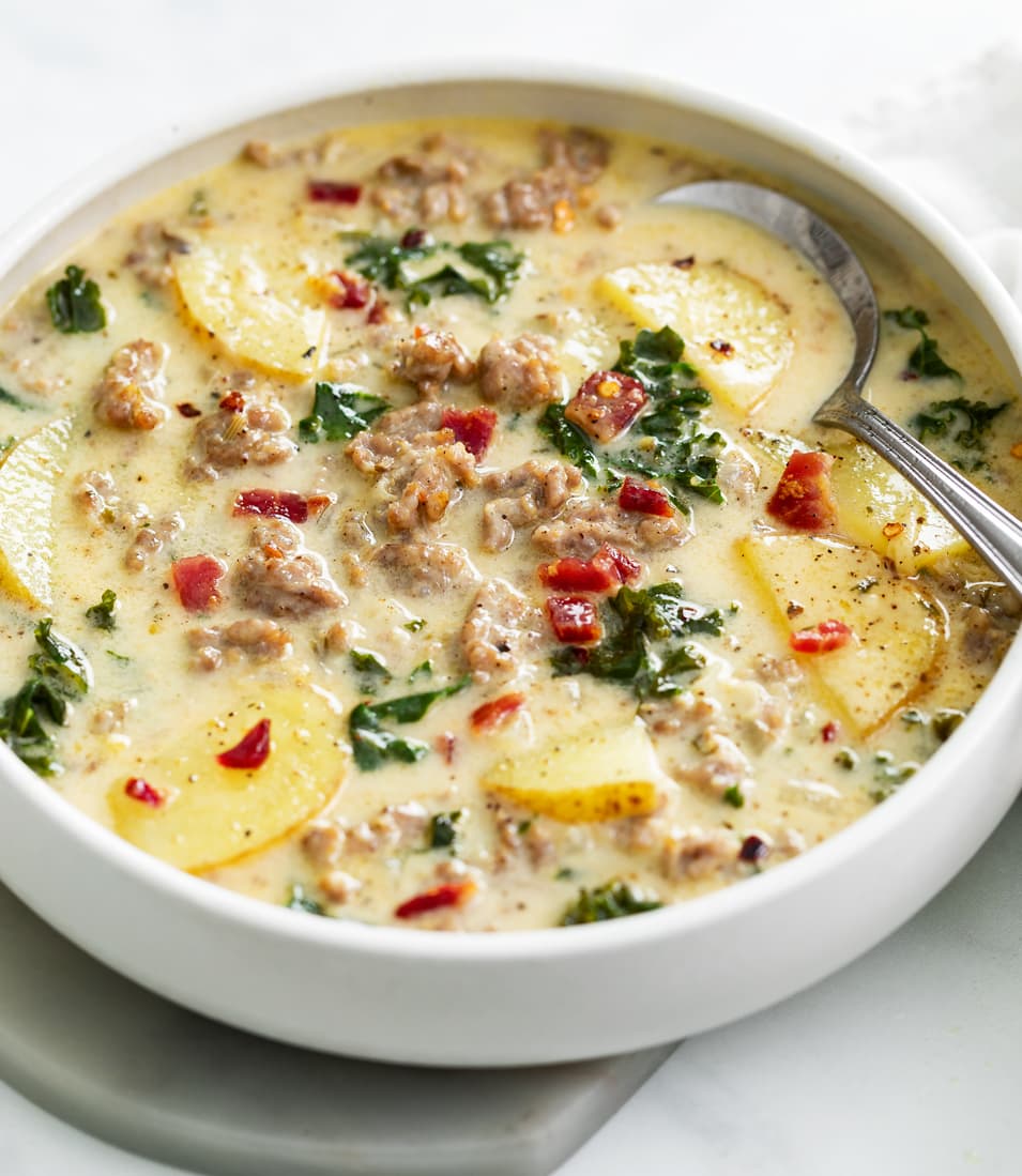 A white bowl of Zuppa Toscana Soup with bacon on top.