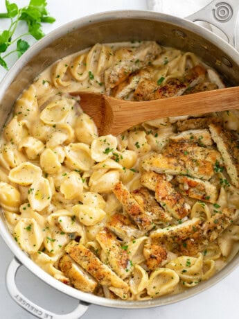 Creamy Chicken Pasta in a skillet with a wooden spoon and chopped parsley.