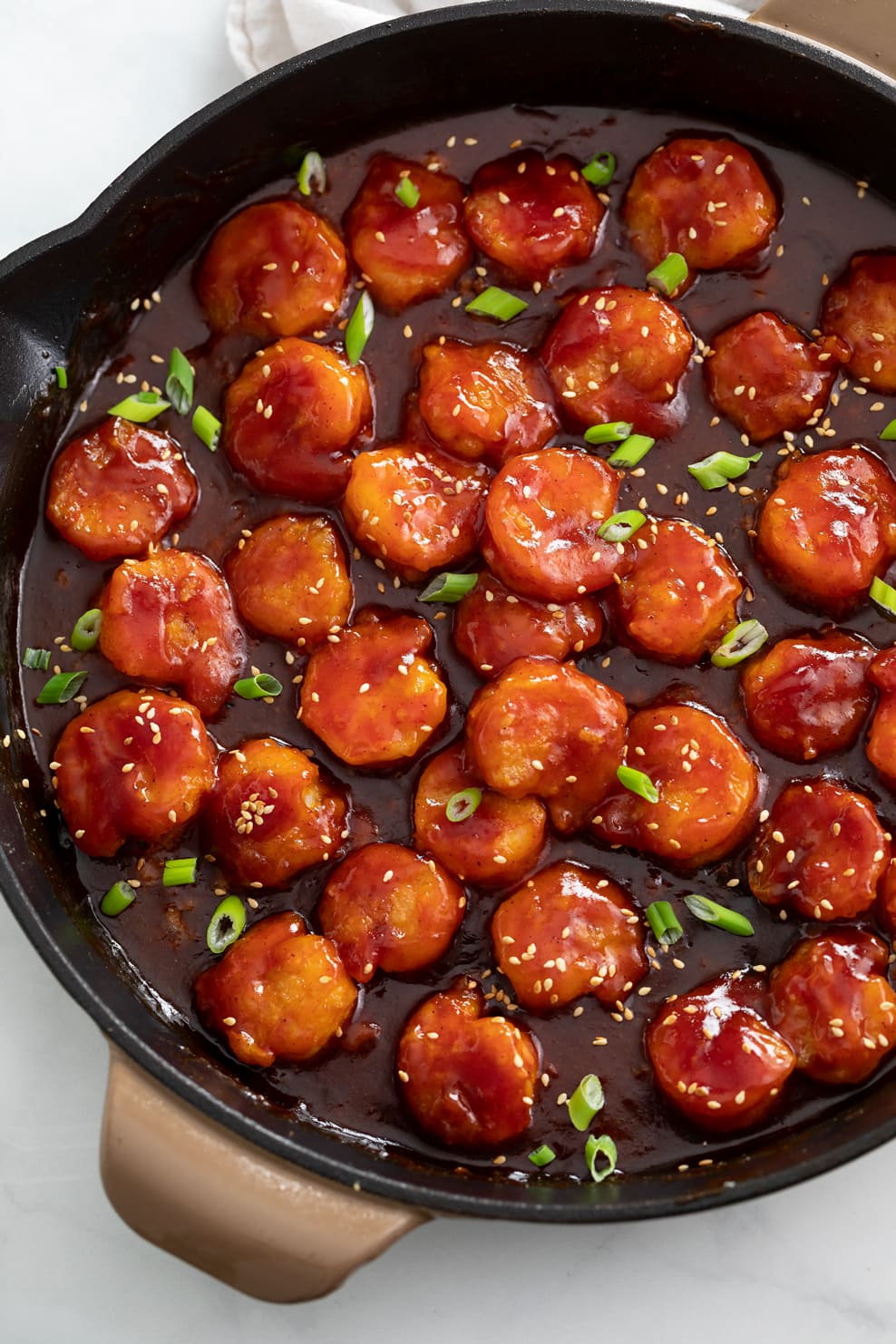 A skillet of Firecracker Shrimp with green onions and sesame seeds on top.