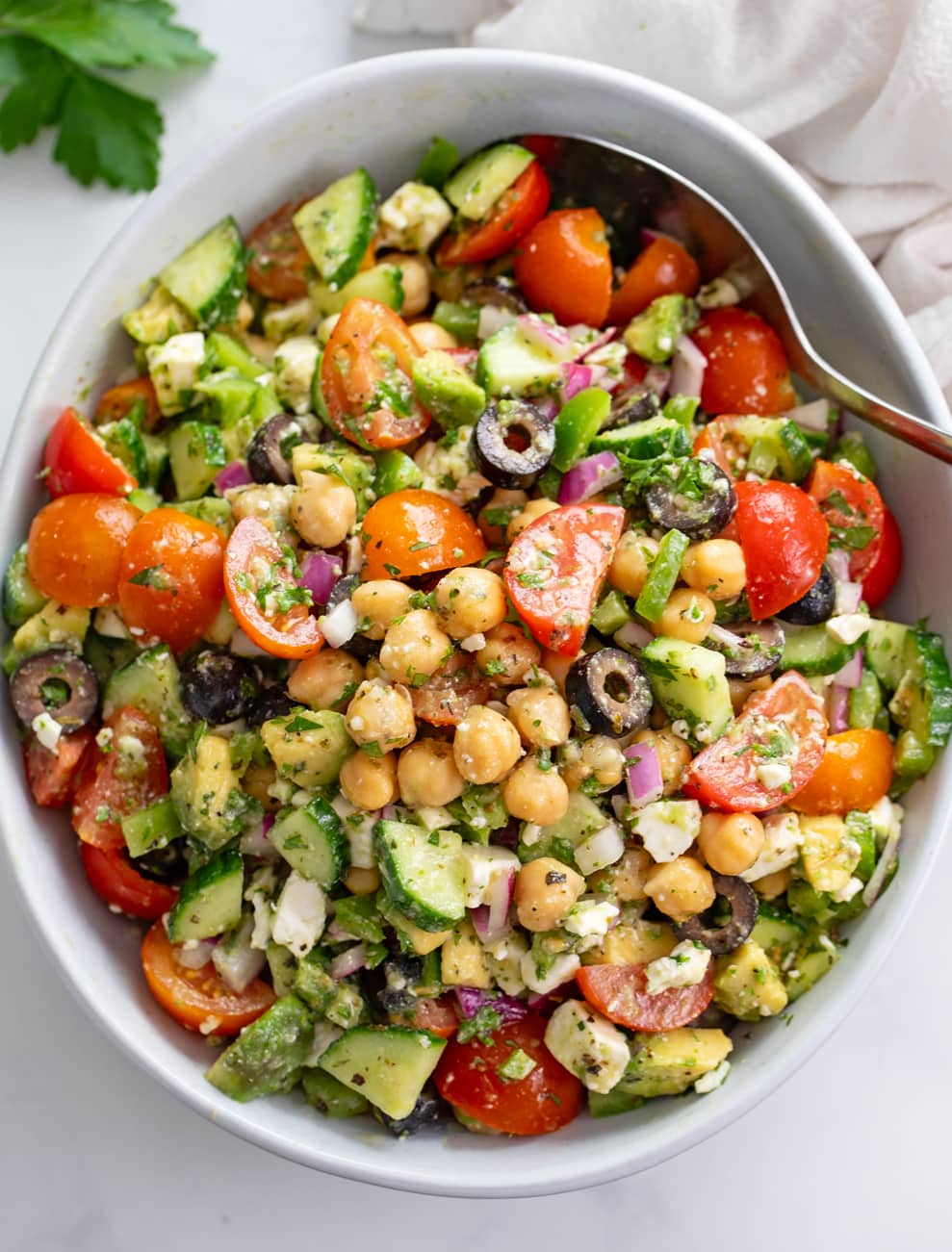 Chickpea Salad in a white bowl with a spoon on the side and dressing on top.