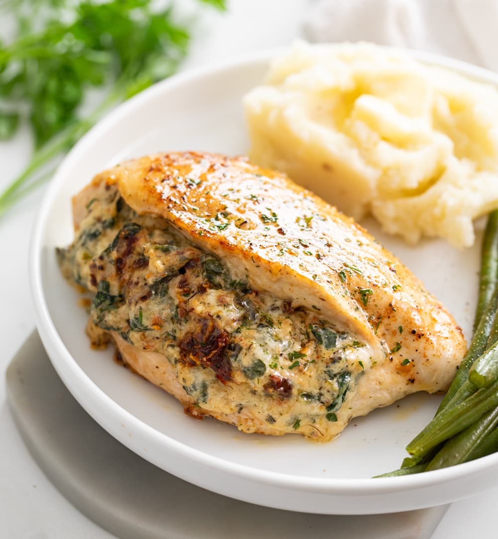 Stuffed Chicken Breast with mashed potatoes in the background and green beans on the side.