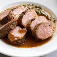 Sliced of Roasted Pork Tenderloin on a white plate with fresh thyme in the back.