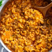 Beefaroni in a skillet with a wooden spoon scooping it up.