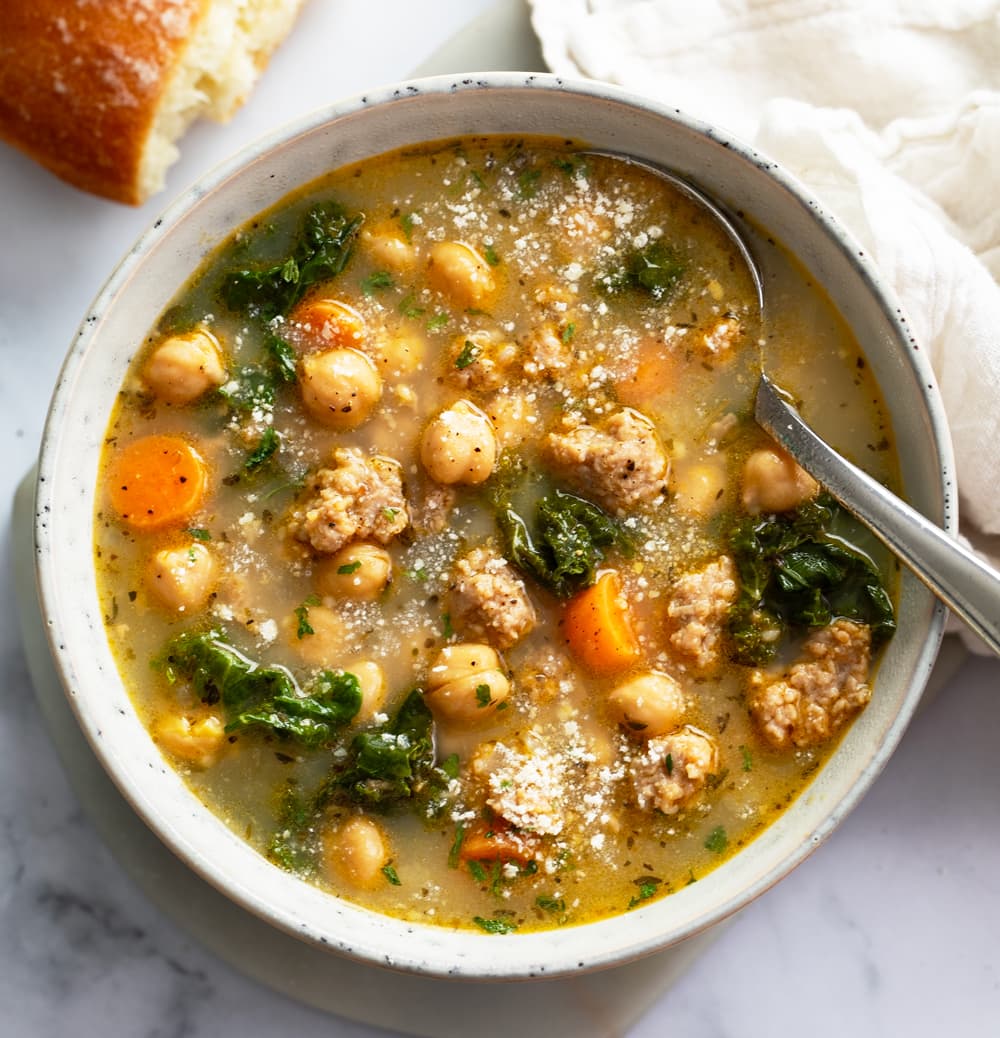 A bowl of Chickpea Soup with a spoon on the side and Parmesan cheese on top.
