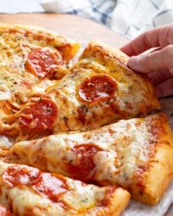 A hand pulling up a slice of cheesy pepperoni pizza.