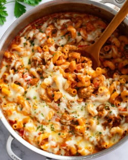 Italian Sausage Pasta in a skillet with a wooden spoon scooping it up.