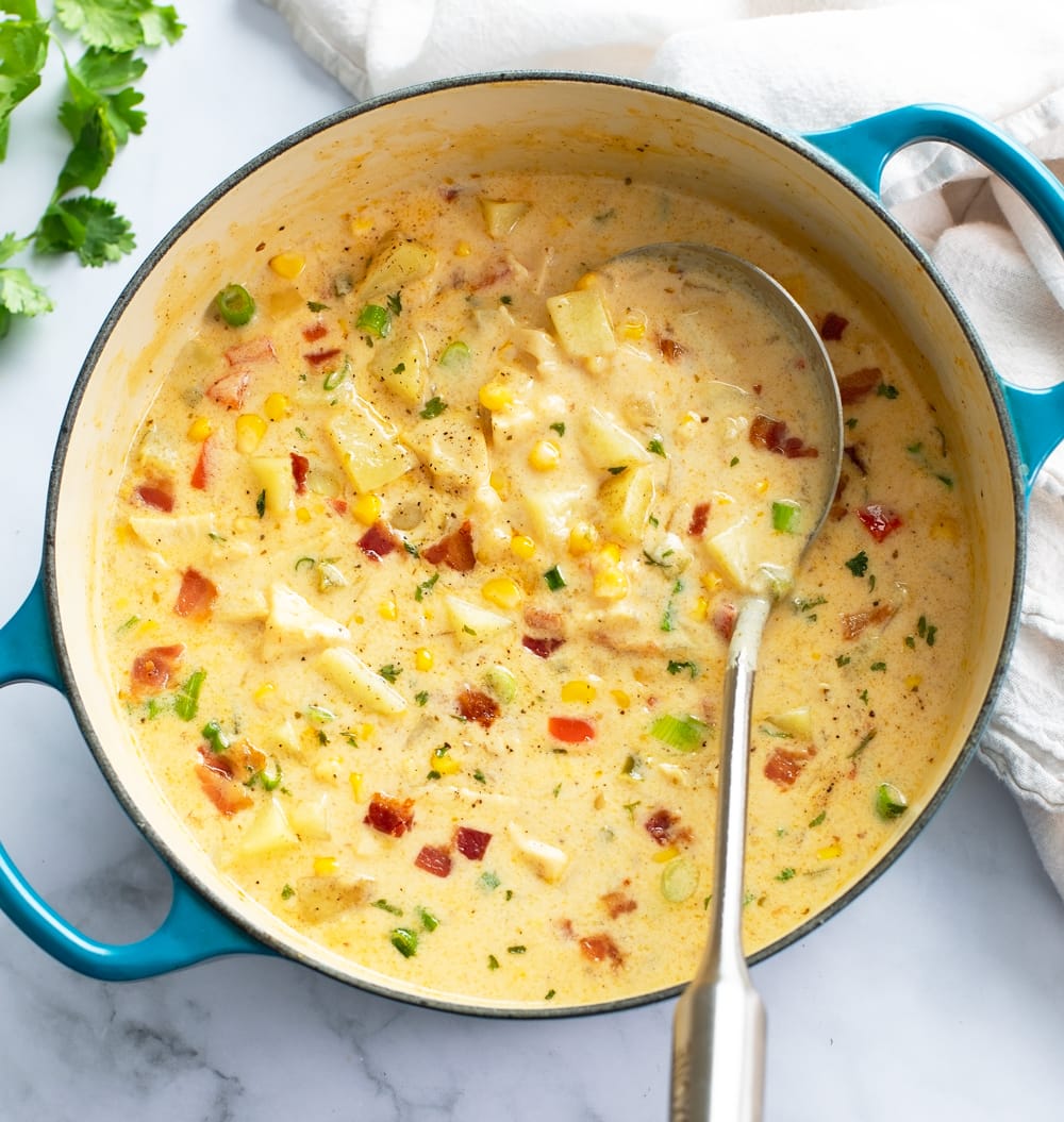 Chicken Corn Chowder in a blue soup pot with a ladle on the side and bacon and chives on top.