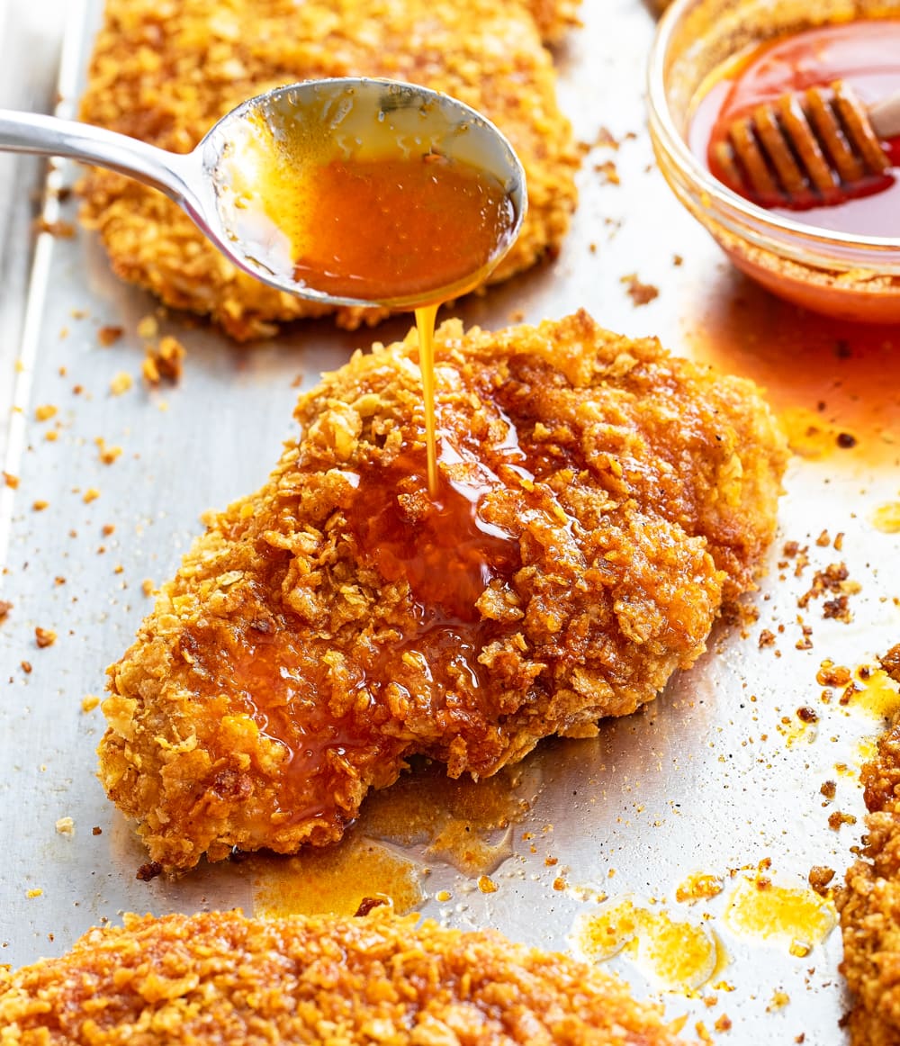 A spoon drizzling honey on top of crispy chicken.
