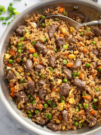 Beef Fried Rice in a skillet with peas and carrots and a spoon.