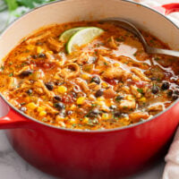 A red soup pot filled with Chicken Taco Soup with a spoon on the side.