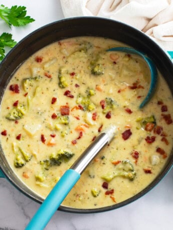 A soup pot of Broccoli Potato Soup with bacon on top and a ladle on the side.