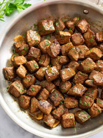 Steak Bites in a skillet in a Garlic Butter Sauce with parley on top.