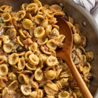 A wooden spoon scooping up French Onion Pasta from a skillet.