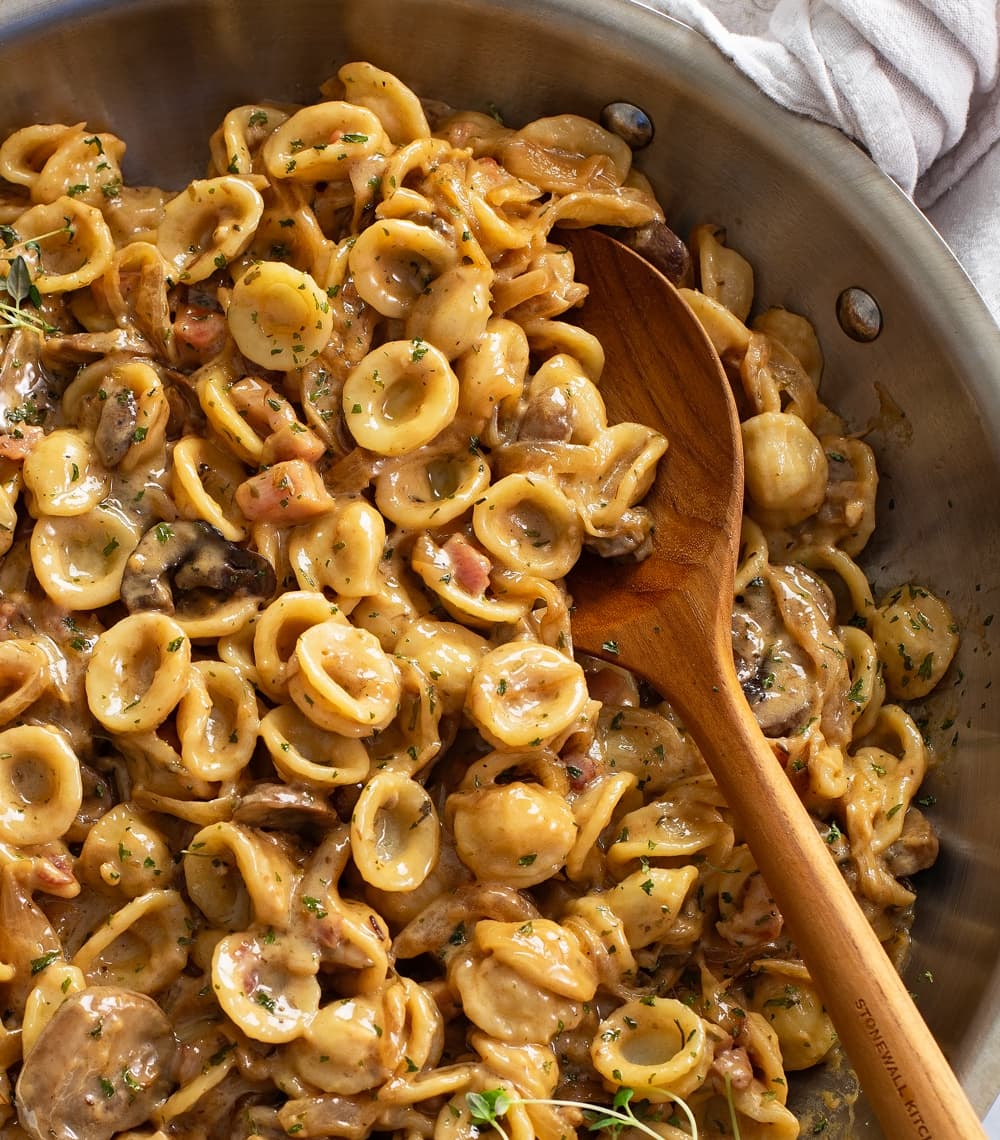 A wooden spoon scooping up French Onion Pasta from a skillet.