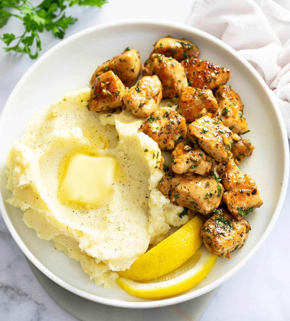 Chicken Bites on a white plate next to mashed potatoes and lemon wedges.
