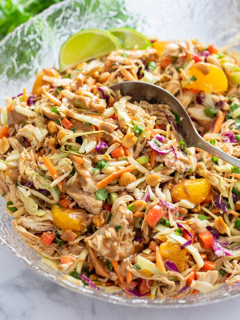 Thai Chicken Salad in a glass bowl with a spoon scooping it up.